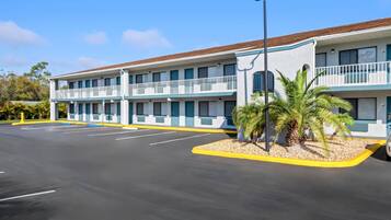Un motel de dos pisos, con estacionamiento y una pequeña palmera.