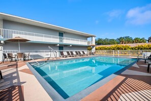 A rectangular swimming pool with a tiled edge, surrounded by lounge chairs and a covered seating area.