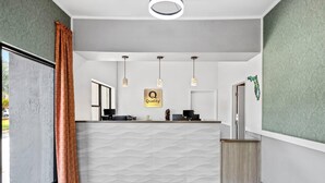 Un comptoir d’accueil avec une pancarte indiquant « Qualité », des suspensions, un mur décoré d’un motif et une fenêtre avec des rideaux.