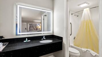 A bathroom with a black countertop, a white sink, a mirror with lights, a white toilet, and a yellow shower curtain.
