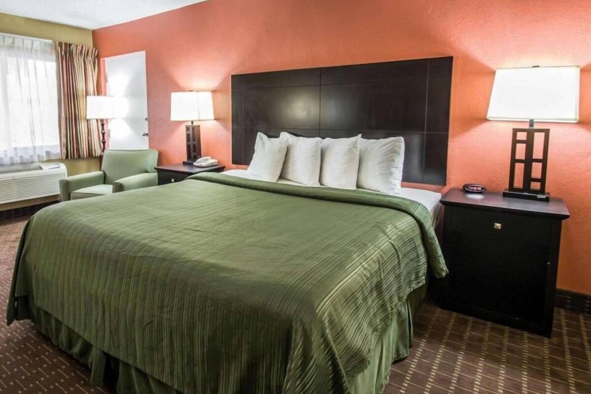 A hotel room with a large bed, two bedside tables with lamps, a headboard, and a window with curtains.
