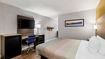 A hotel room with a bed, desk, chair, television, and artwork on the wall.