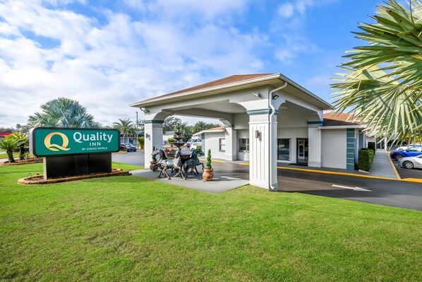 A Quality Inn by Choice Hotels with a covered entrance, palm trees, and a clear sky.