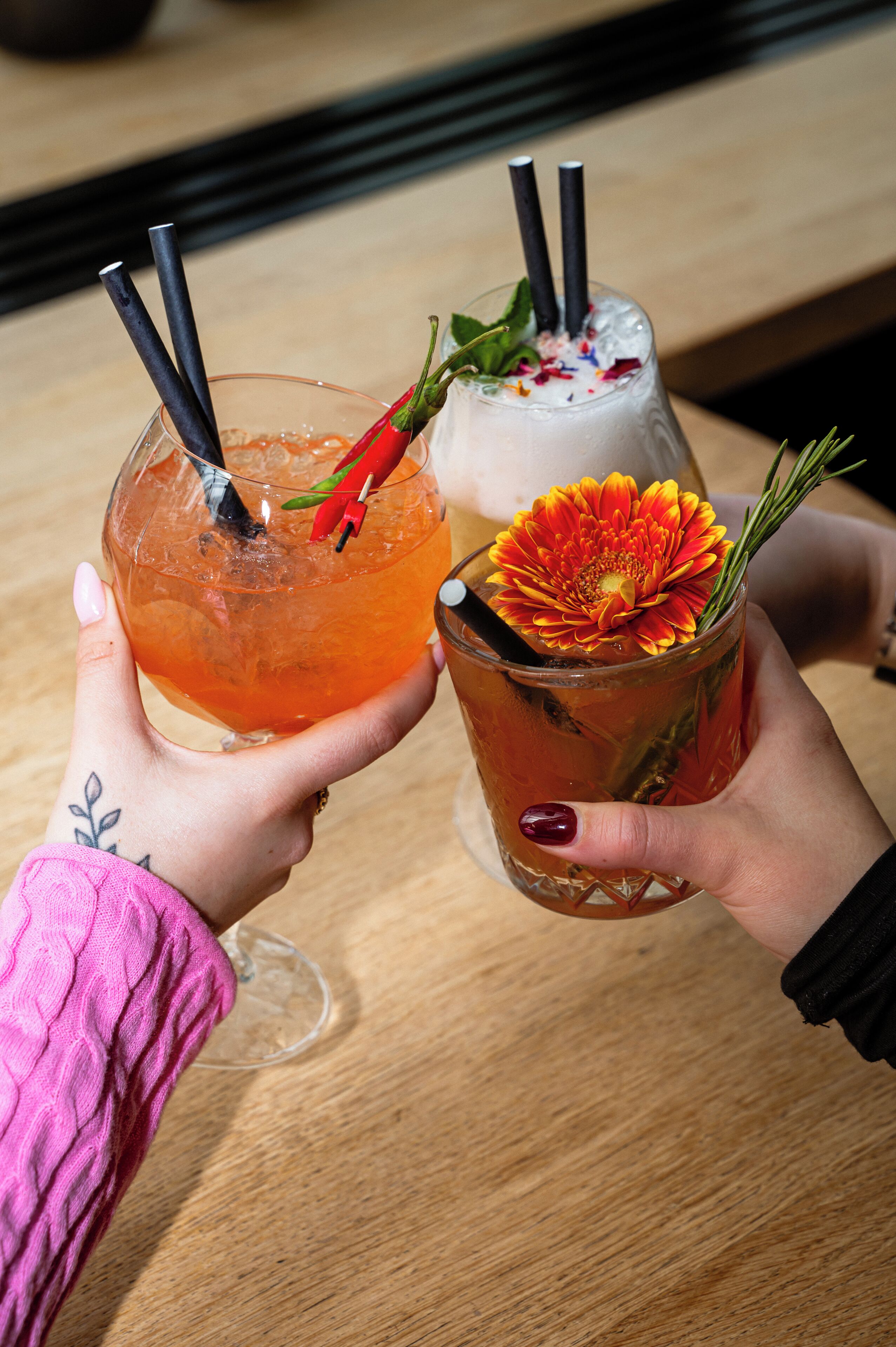 Two hands holding glasses of drinks with straws and garnishes.