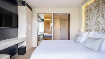 Une chambre d’hôtel moderne dotée d’un grand lit, d’un téléviseur fixé au mur, d’une salle de bain avec un miroir et un lavabo, et d’une tête de lit à motifs.