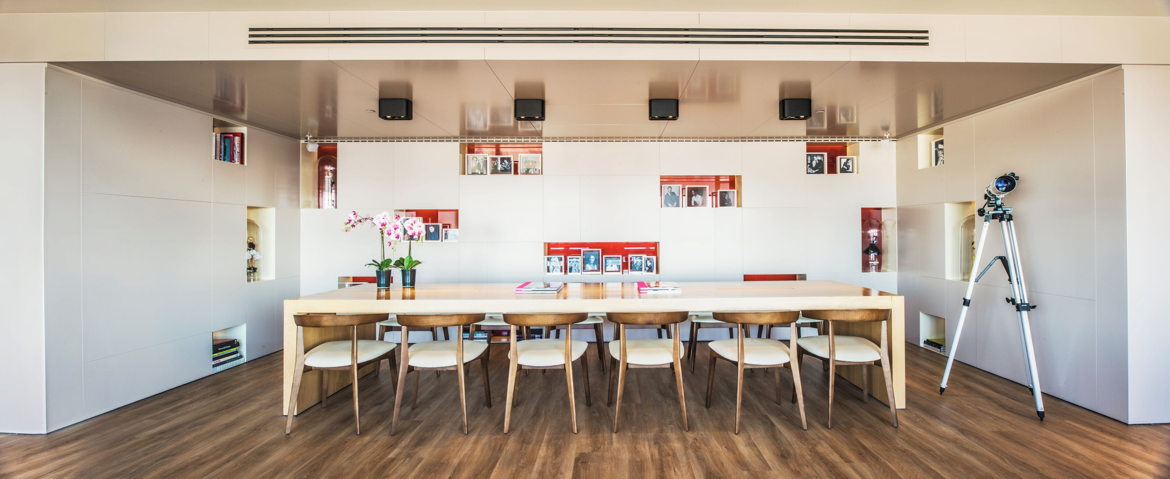 A modern meeting room with a long table, six chairs, and a tripod on the right.