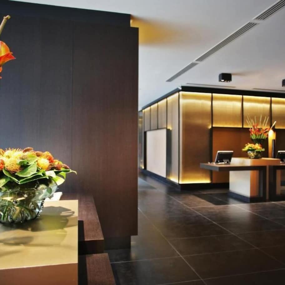 A modern hotel lobby with a reception desk, a large vase of flowers, and a seating area.