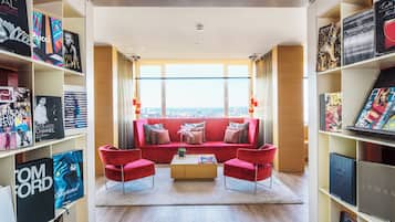 A modern living room with a red sofa, a coffee table, and bookshelves filled with magazines and books.