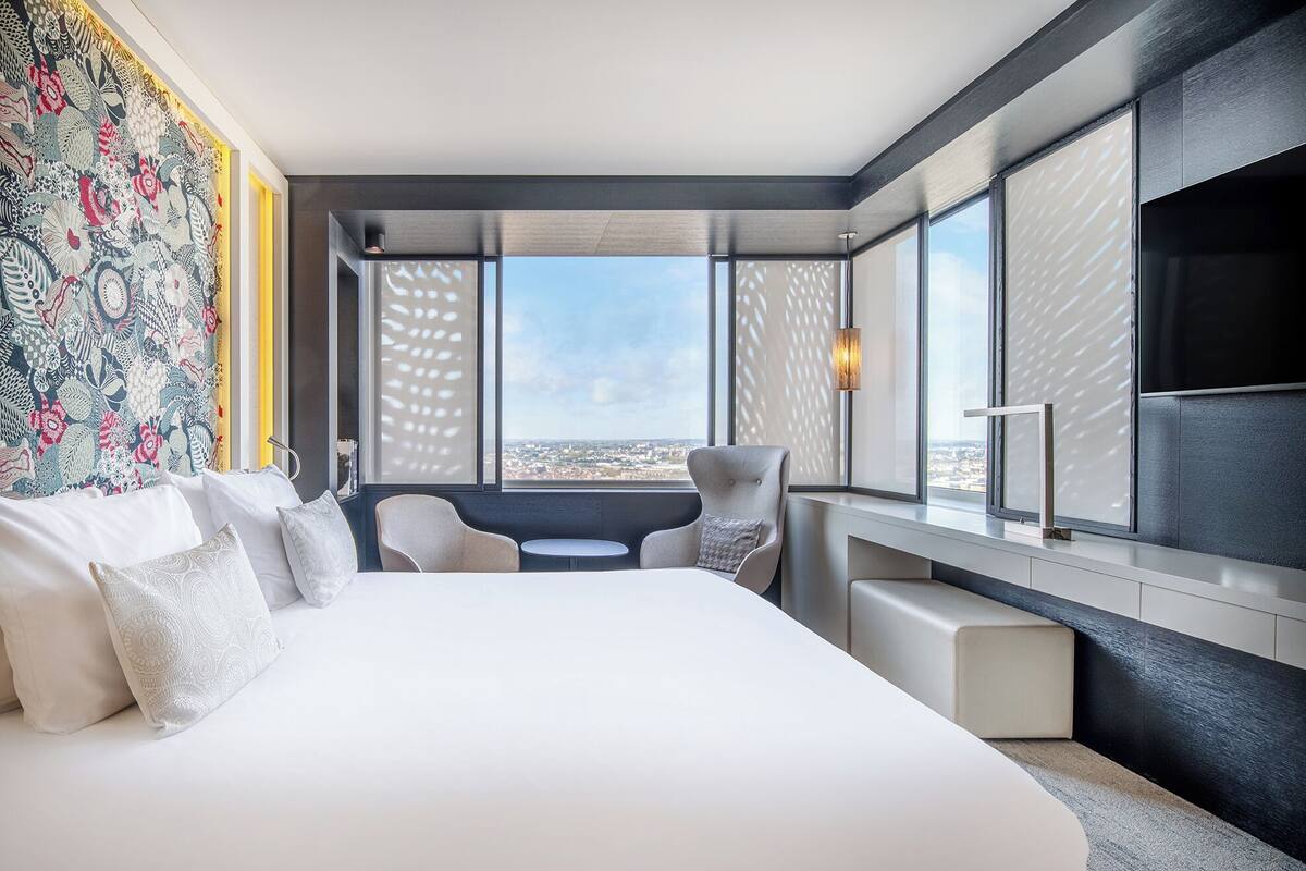 A modern hotel room with a large bed, a desk, and a view of the city.