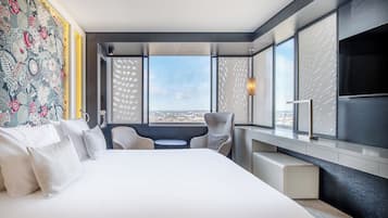 A modern hotel room with a large bed, a desk, and a view of the city.