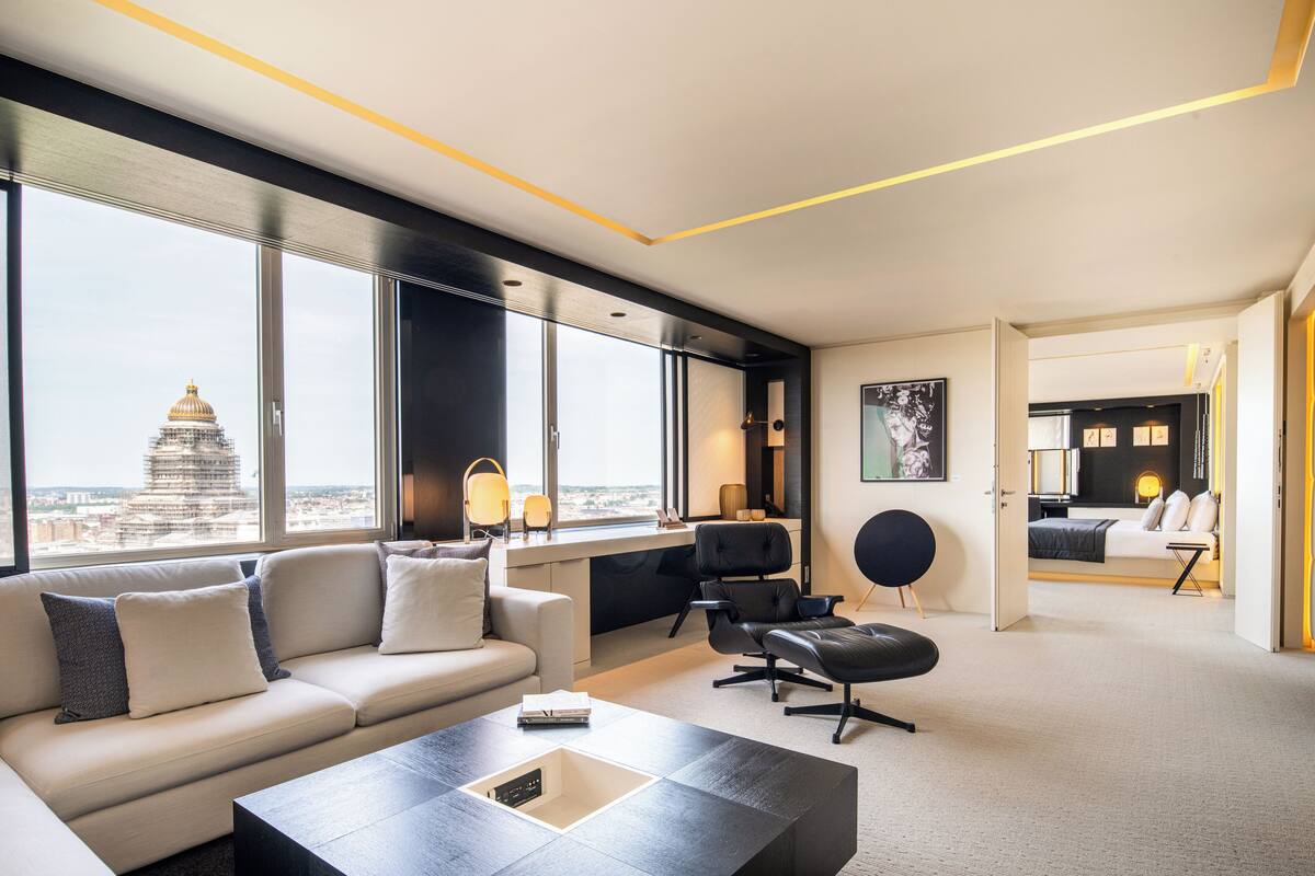 A modern hotel room with a large window, a sofa, a desk, and a bed.