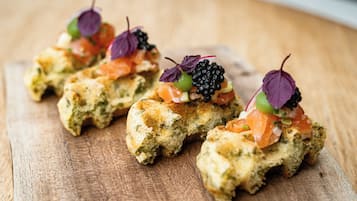 Tres bruschettas con salmón, moras y hojas verdes sobre una tabla de madera.
