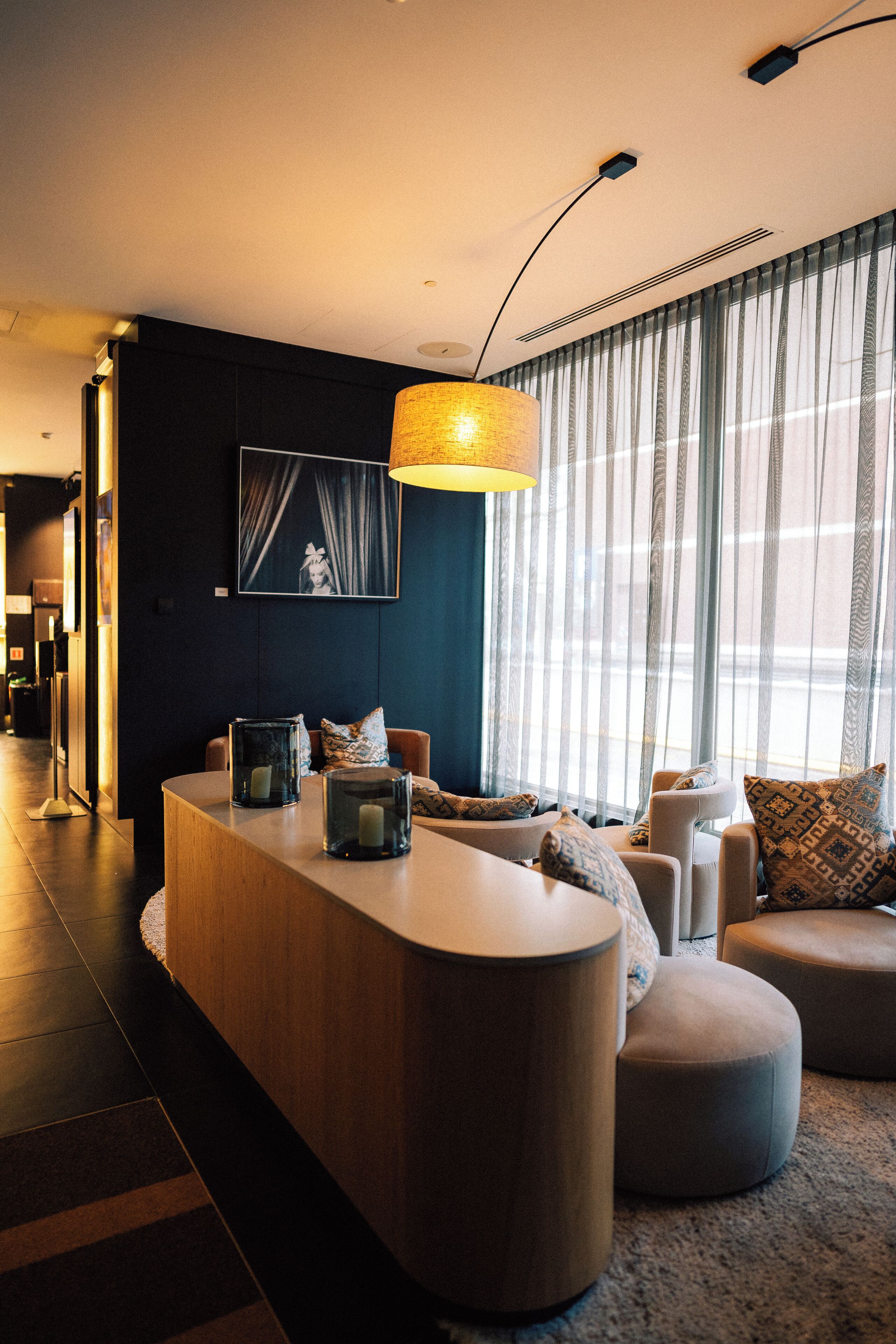 A modern living room with a curved wooden coffee table, a sofa, and a large window with sheer curtains.