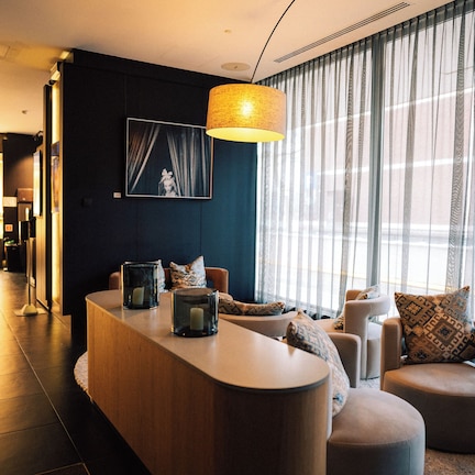 A modern living room with a curved wooden coffee table, a sofa, and a large window with sheer curtains.