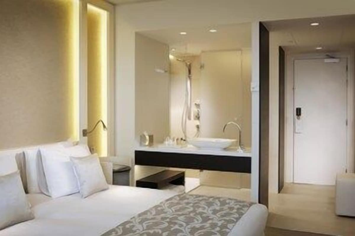 Una habitación de hotel moderna con una cama grande, un tocador con espejo, ducha y puerta separada.
