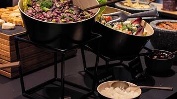 Un buffet proposant divers plats, notamment un grand saladier de salade, des bols d’oignons marinés et un bol de sauce verte.