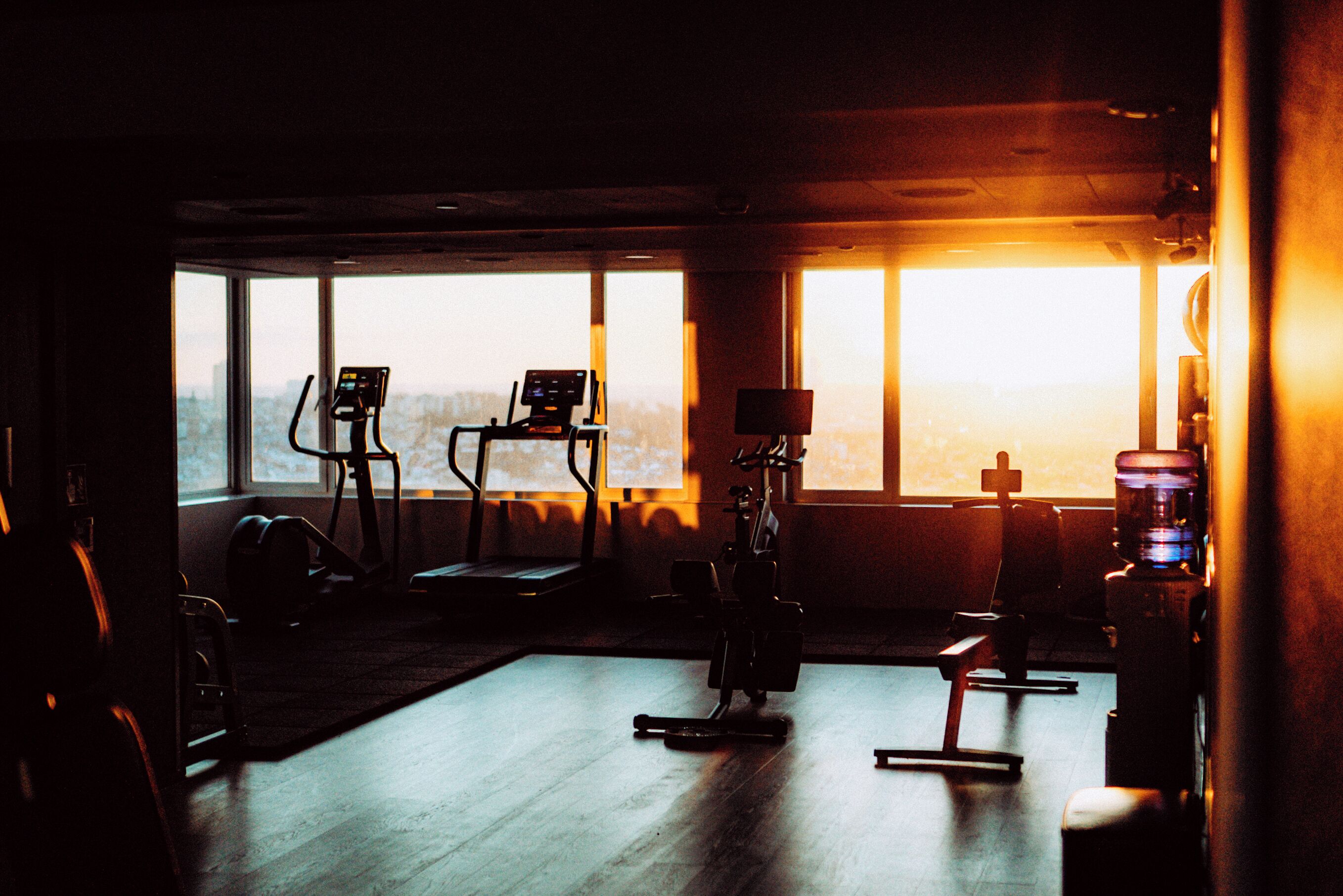 Une salle de sport équipée de matériel d’exercice, dotée de grandes fenêtres et offrant une vue sur la ville.