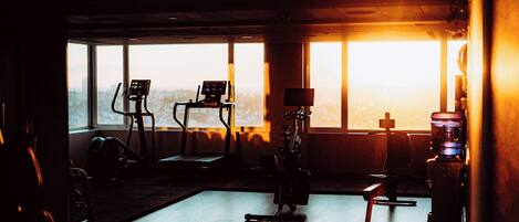 Une salle de sport équipée de matériel d’exercice, dotée de grandes fenêtres et offrant une vue sur la ville.