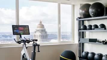 A gym with an exercise bike, a large exercise ball, and a shelf with multiple exercise balls. A large window provides a view of a dome-shaped building.