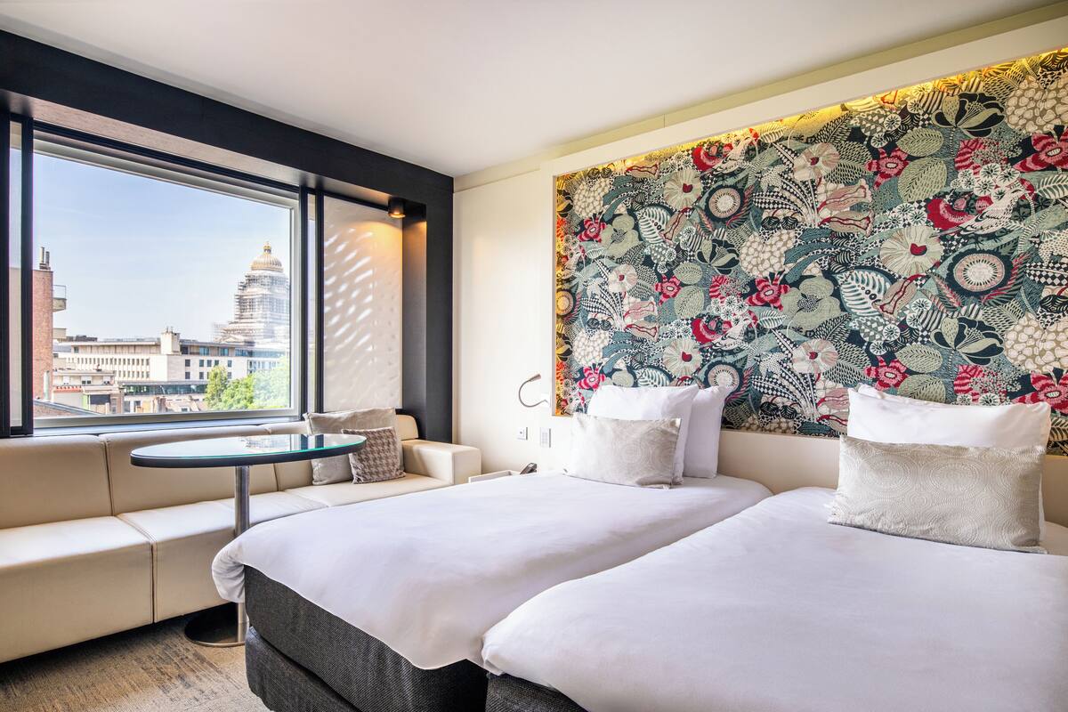 A hotel room with a large window, a sofa, a bed, and a decorative wall.