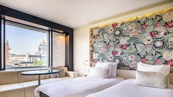 A hotel room with a large window, a sofa, a bed, and a decorative wall.