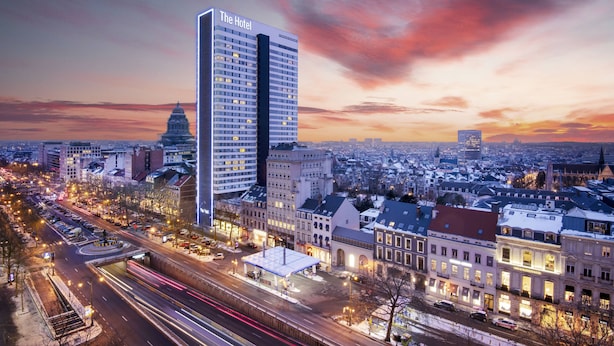 Un hotel modern d'alçada elevada, envoltat d'edificis històrics i un paisatge urbà durant el crepuscle.