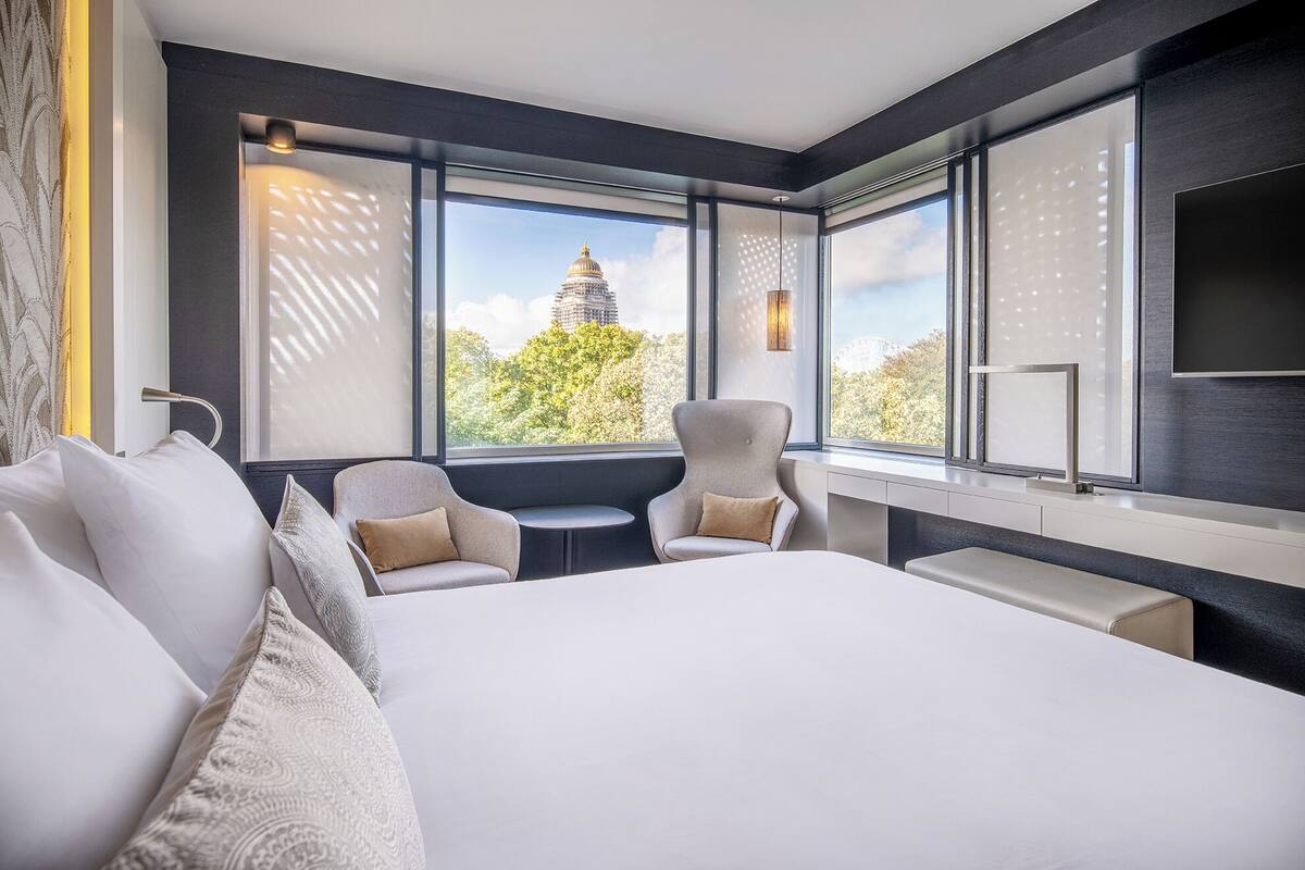 A modern hotel room with a large bed, two armchairs, a small table, and a TV.