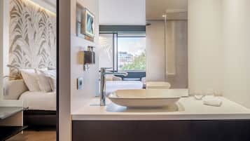 Een moderne badkamer met een groot wastafelmeubel, een spiegel en een raam met uitzicht op de stad.