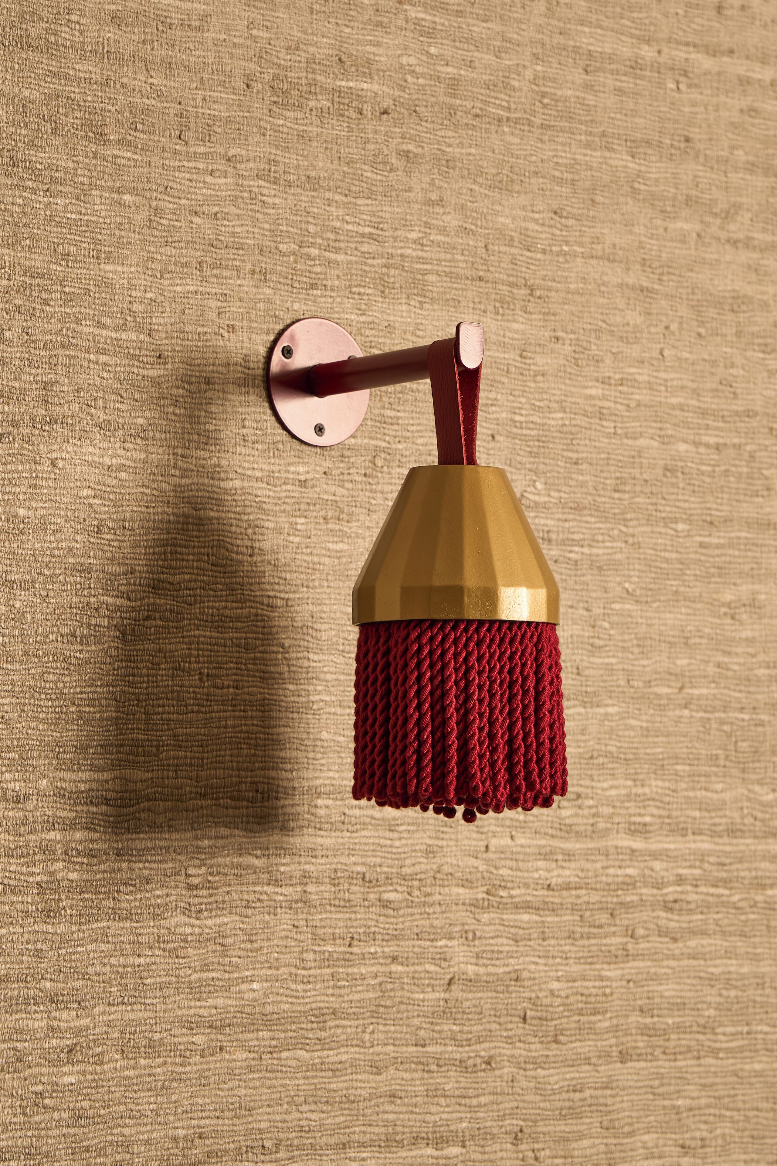 Une serpillière murale avec un manche rouge et une tête dorée, fixée à un mur beige à texture.