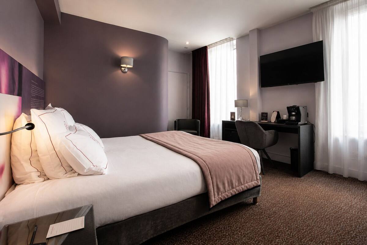 Habitación de hotel con cama, escritorio, televisor de pantalla plana y cafetera.