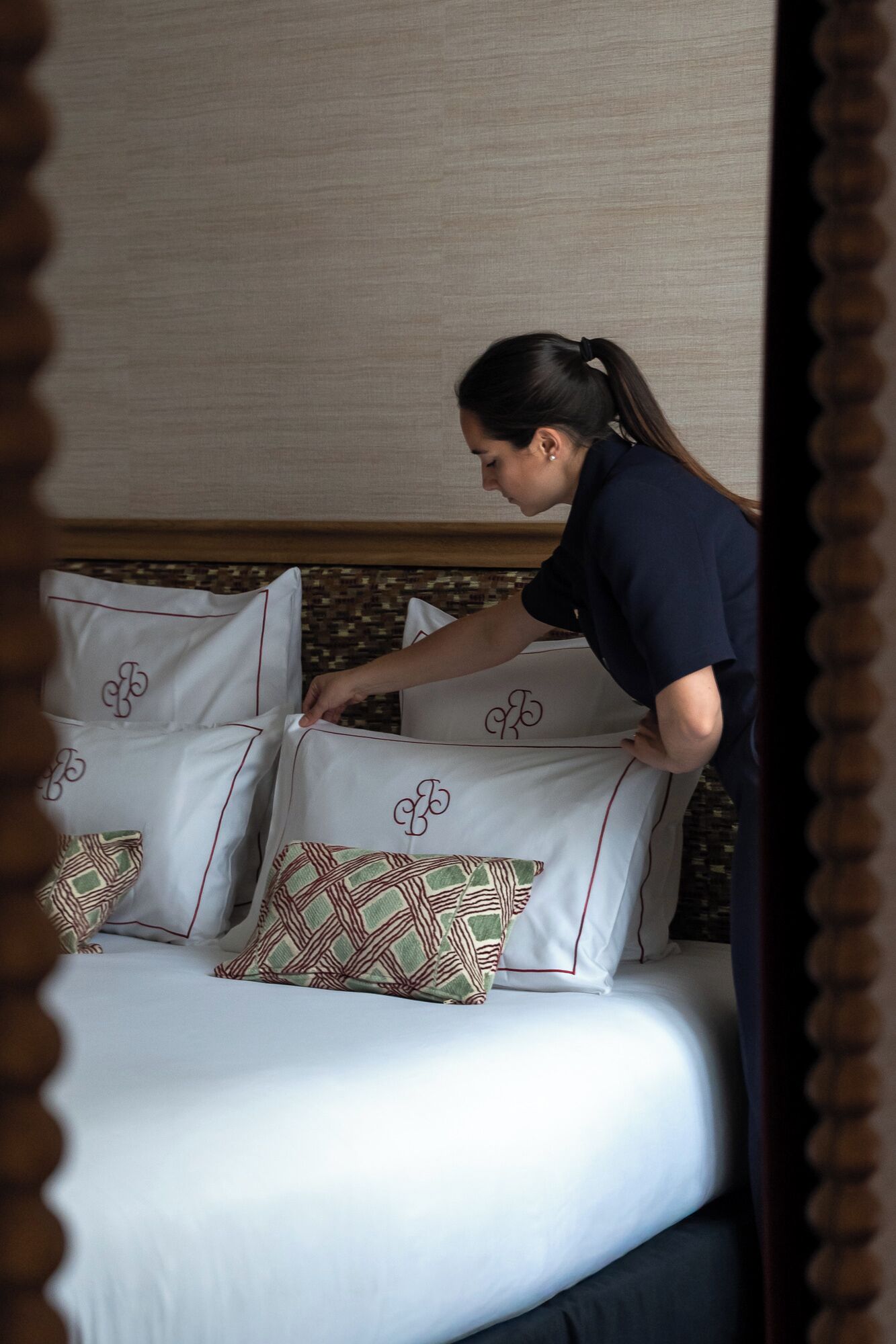 Una persona acomodando almohadas en una cama, con una almohada estampada y otra lisa.