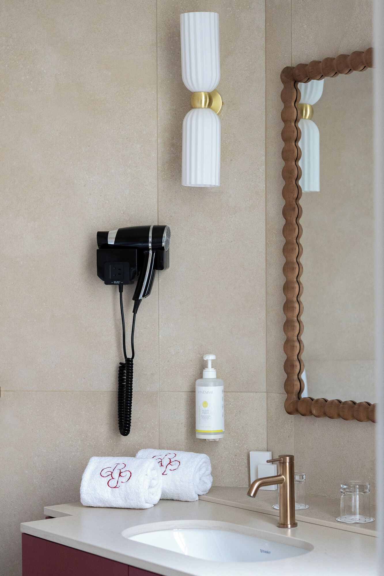 Un baño con secador de pelo, toalla, dispensador de jabón y un espejo con marco de madera.