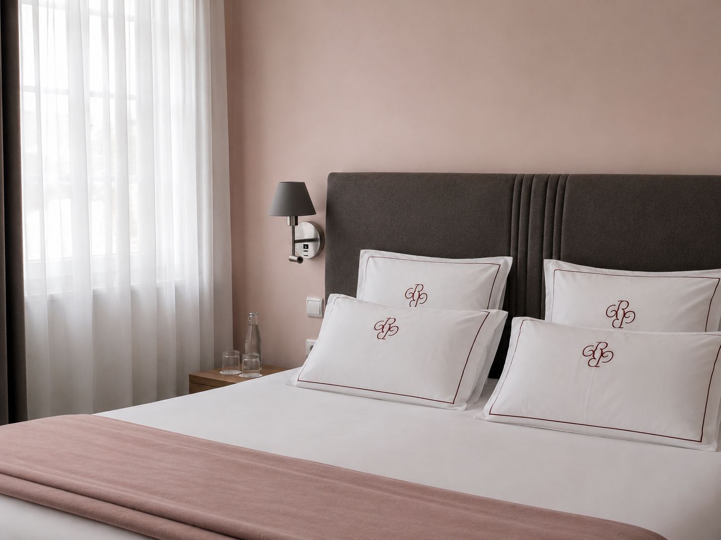 A hotel room with a bed, pillows, a nightstand, a lamp, and a window with curtains.