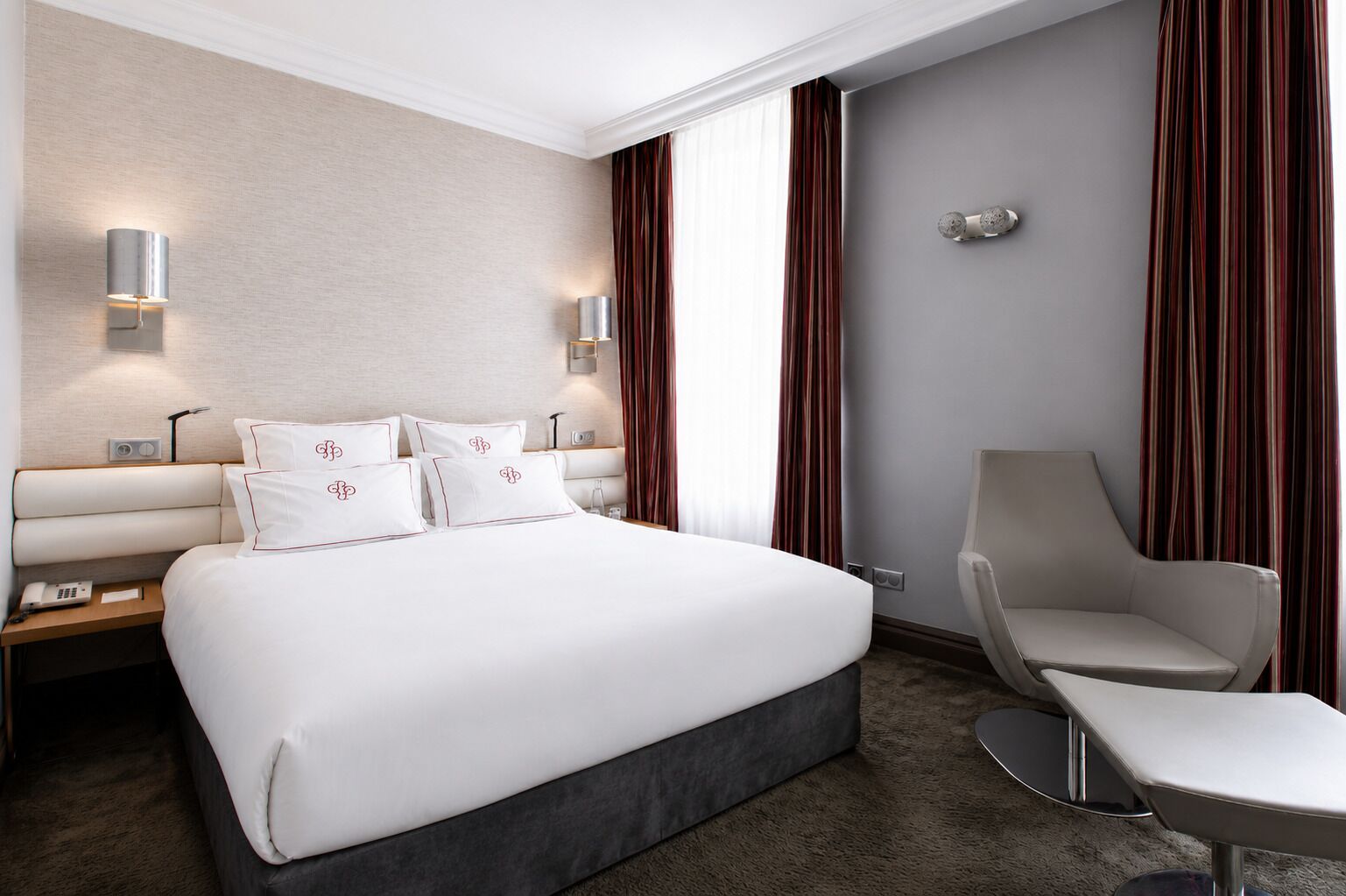 Une chambre d’hôtel avec un grand lit, des lampes de chevet, une chaise et une fenêtre avec des rideaux.
