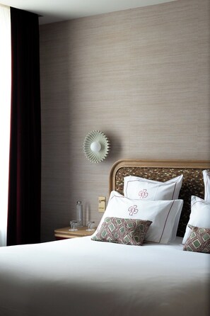 A hotel room with a bed, pillows, a bedside table, a lamp, and a window with curtains.