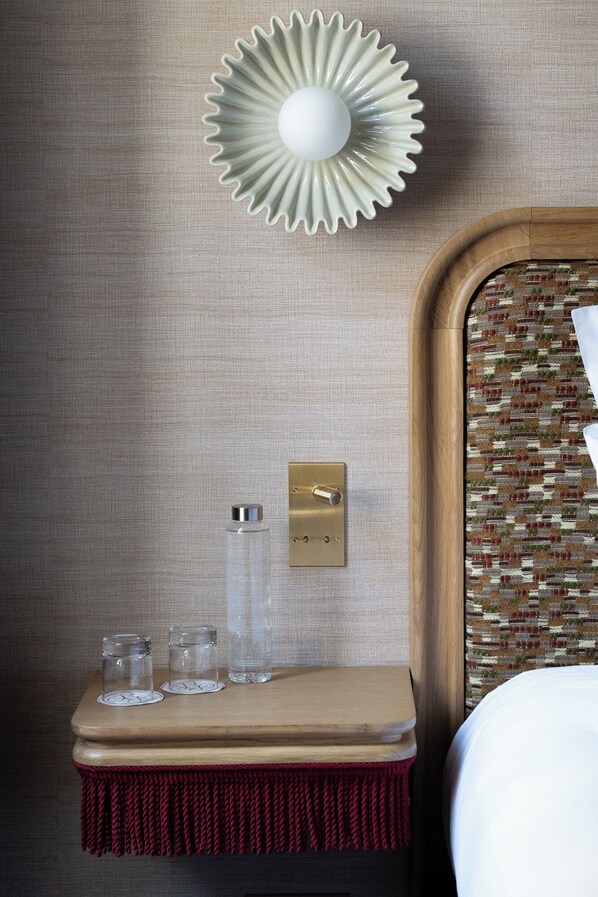 A wooden bedside table with a red fringe, a wall-mounted light fixture, and a textured wall.
