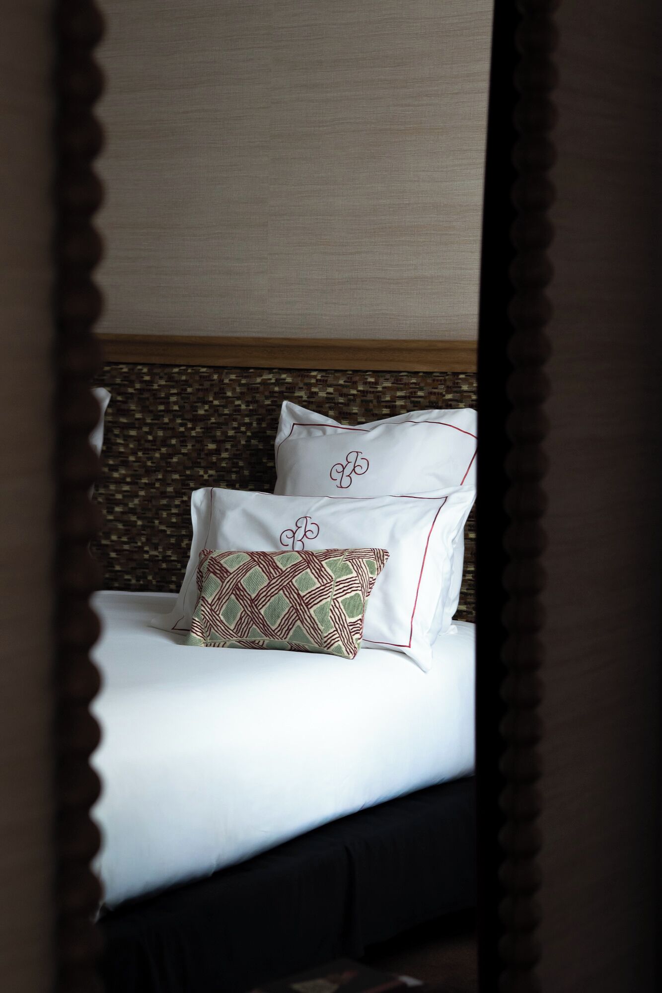 A bed with white linens, two pillows with embroidered initials, and a patterned pillow.