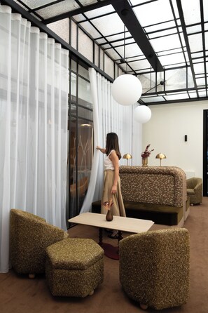 A room with a glass partition, a sofa, two ottomans, a table, and a hanging light fixture.