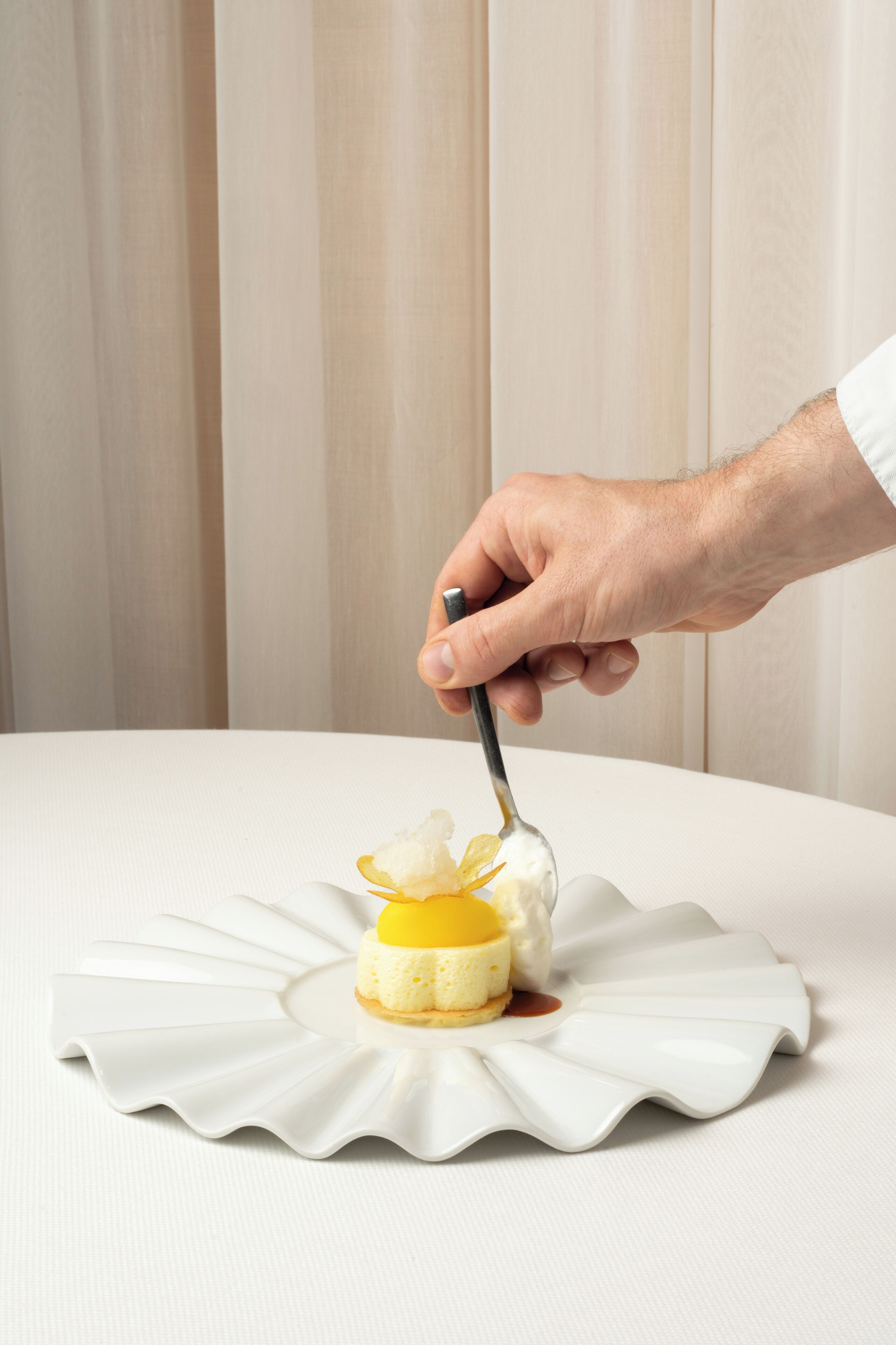A hand holding a spoon over a dessert on a white plate.