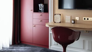 A hotel room with a red wardrobe, a wooden table with a flat-screen TV, and a small minibar.