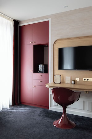 Een hotelkamer met een rode kast, een houten tafel met een flatscreen televisie en een klein minibar.