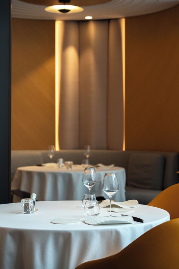 A restaurant with round tables, white tablecloths, and a warm ambient light.