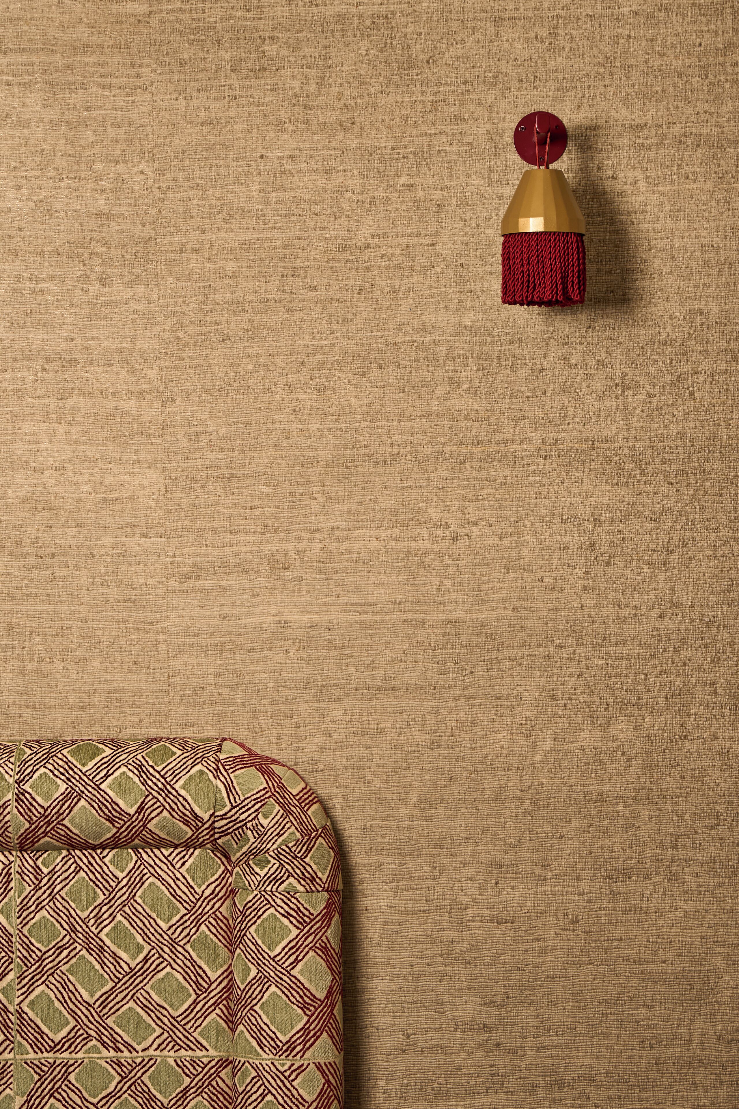 Un mur à la texture particulière, agrémenté d’une frange rouge suspendue et d’un coussin à motifs.
