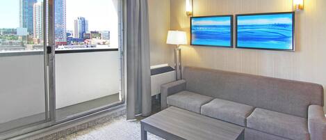 A hotel room with a balcony, a sofa, a table, and two wall-mounted televisions.