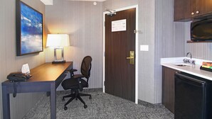 A hotel room with a wooden desk, a chair, a lamp, a telephone, a microwave, and a refrigerator. - Holiday Inn Express Hotel & Suites Calgary by IHG (Calgary)