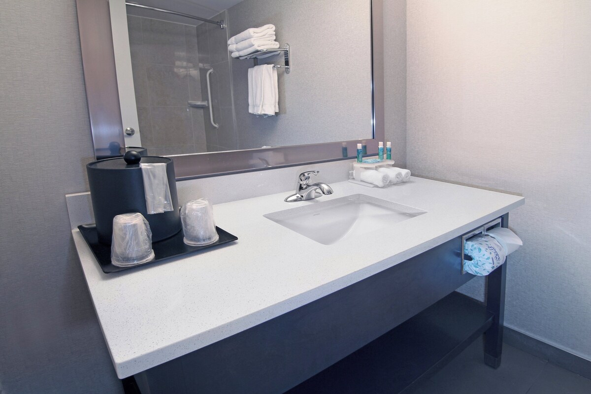 A modern bathroom with a white sink, a large mirror, and a towel rack.