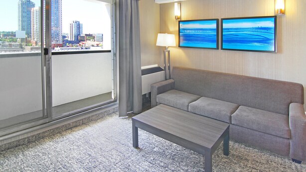 A hotel room with a balcony, a grey sofa, a small table, and two wall-mounted paintings. - Holiday Inn Express Hotel & Suites Calgary by IHG (Calgary)