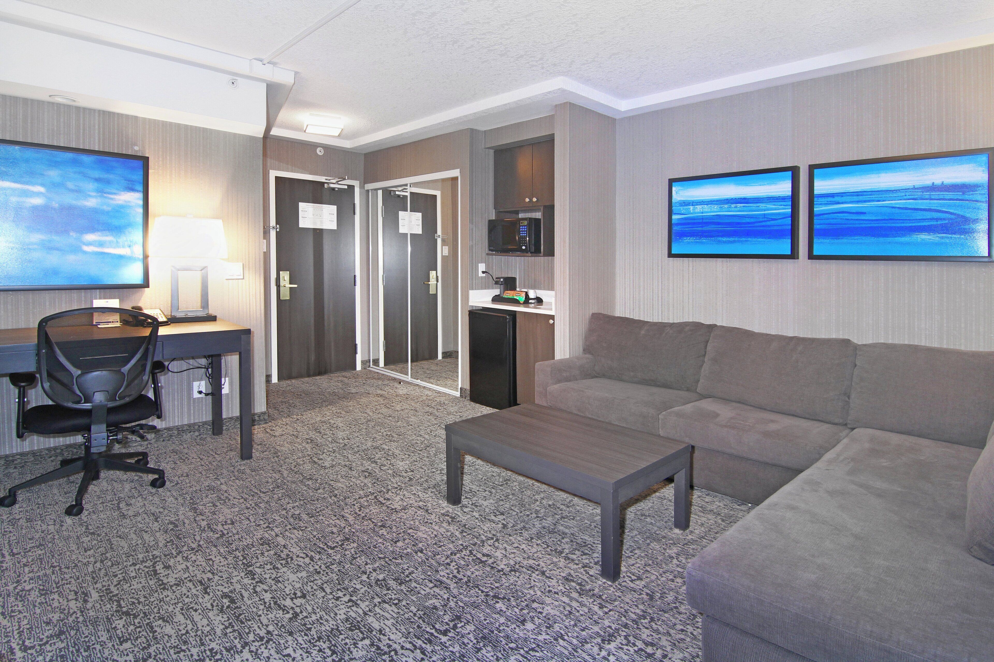 A hotel room with a desk, chair, sofa, coffee table, and artwork on the walls.