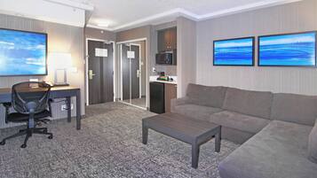 A hotel room with a desk, chair, sofa, coffee table, and artwork on the walls.