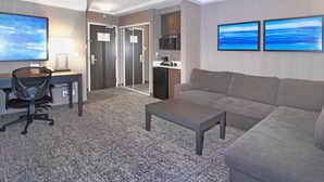 A hotel room with a gray sofa, a desk with a computer, a TV, and two framed pictures on the wall. - Holiday Inn Express Hotel & Suites Calgary by IHG (Calgary)